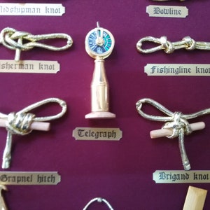 Detail view of golden sailor's knots, miniature naval tools, golden cardboard labels and red fabric background.