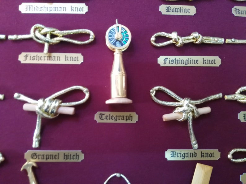 Detail view of golden sailor's knots, miniature naval tools, golden cardboard labels and red fabric background.