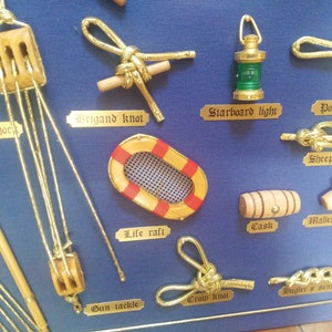 Detail view of table with golden knots and miniatures of naval tools, fabric background and golden cardboard labels.