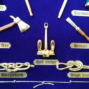 Detail view of golden sailor's knots, miniature naval tools, golden cardboard labels and blue fabric background.