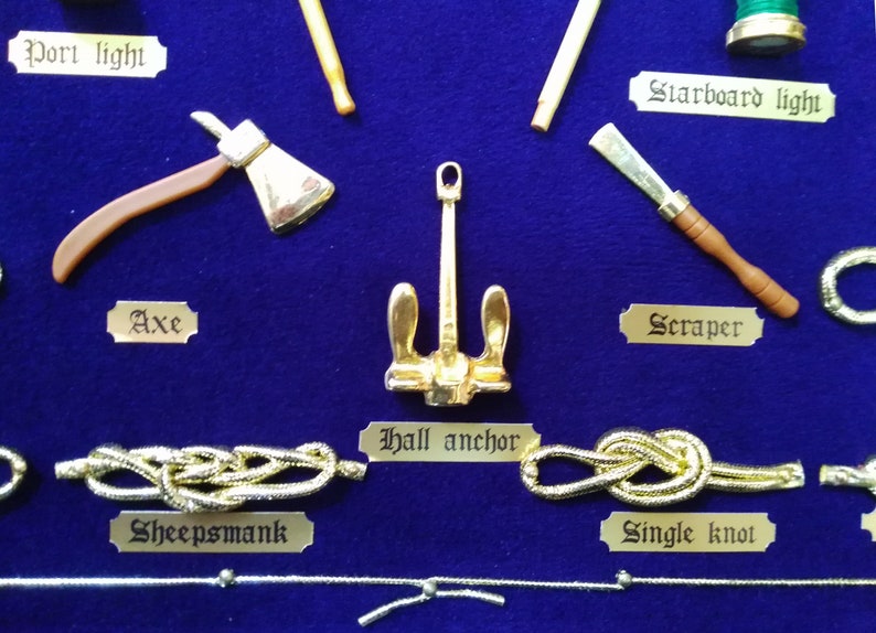 Detail view of golden sailor's knots, miniature naval tools, golden cardboard labels and blue fabric background.