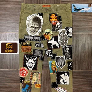 May include: Green cargo trousers with a variety of patches sewn on. The patches feature images of skulls, monsters, and other graphic designs. Some of the text on the patches includes "City Morgue", "Ghetto Rules", "La Planete Sauvage", and "Ken Park".