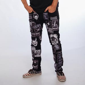 Può includere: Jeans neri con toppe con varie grafiche in bianco e nero, indossati con una maglietta nera, un berretto da baseball azzurro con disegni a croce e scarpe da ginnastica con un motivo a bandiera americana.
