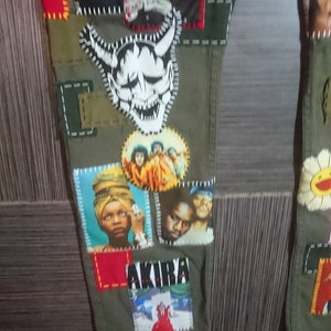 May include: Green cargo pants with various patches sewn on. Patches include a white demon face, a group of people, a woman with a head wrap, a man with a beard, and a red and white graphic with the word "AKIRA".