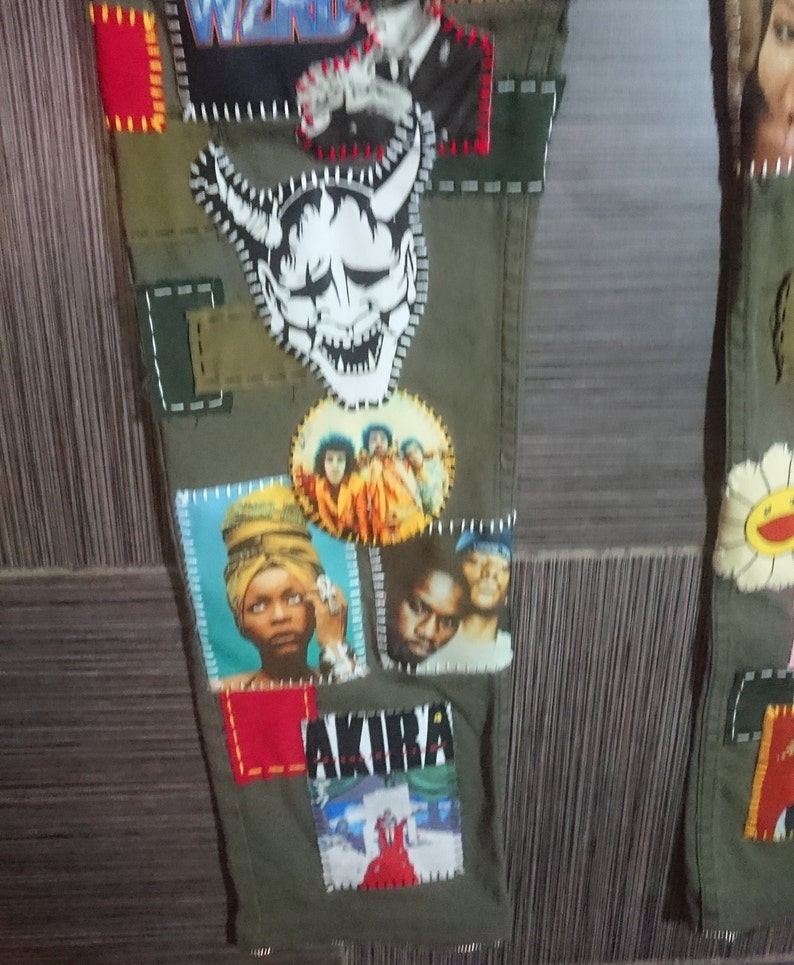 May include: Green cargo pants with various patches sewn on. Patches include a white demon face, a group of people, a woman with a head wrap, a man with a beard, and a red and white graphic with the word "AKIRA".