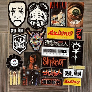 Puede incluir: Una colección de pegatinas con varios personajes de anime, películas y música. Las pegatinas están sobre una superficie de madera. Algunas de las pegatinas incluyen el texto "AKIRA", "EXODUS", "Slipknot", "使徒、殲滅", y "爆裂都市".
