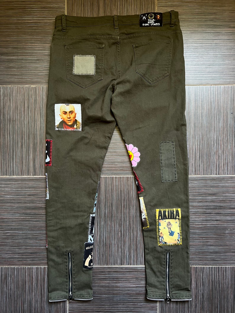 May include: Olive green jeans with various patches, including a flower, a cartoon character, and a portrait of a man. The jeans have zippered hems and a "Sad Sad Sad" patch on the back.