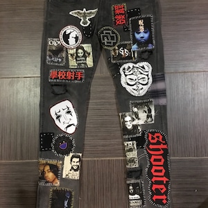 Può includere: Jeans di denim grigi con varie toppe cucite, tra cui un uccello, un teschio, un viso e la parola "shooter" in lettere rosse.