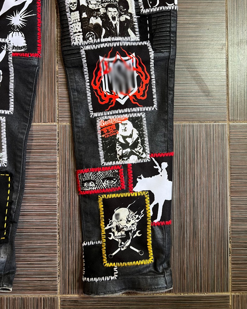 May include: Black denim pants with multiple patches sewn on. The patches feature various designs, including skulls, a cowboy riding a horse, and a person with a red hat. The patches are outlined in white, red, and yellow stitching.