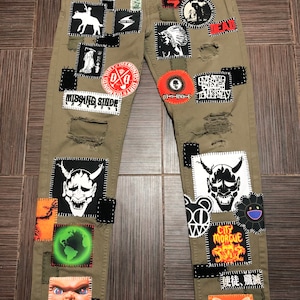 Puede incluir: Pantalón cargo verde con varios parches cosidos. Los parches incluyen una calavera, una mariposa, un demonio, un globo terráqueo y un personaje de la película Child's Play. El pantalón tiene varias roturas y desgarros.