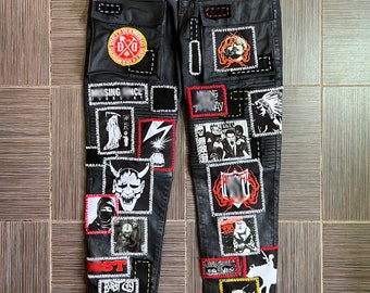May include: Black denim jeans with various patches sewn on. Patches include a skull and crossbones, a demon face, a band logo, and a lightning bolt. The jeans have a distressed look.