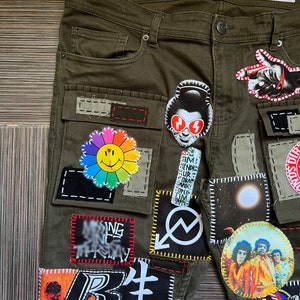 May include: Green cargo pants with various patches sewn on, including a smiley face flower, a red and white graphic, a moon, and a band photo. The pants have a label that reads "W36/L32 DENIM CO. SKINNY".