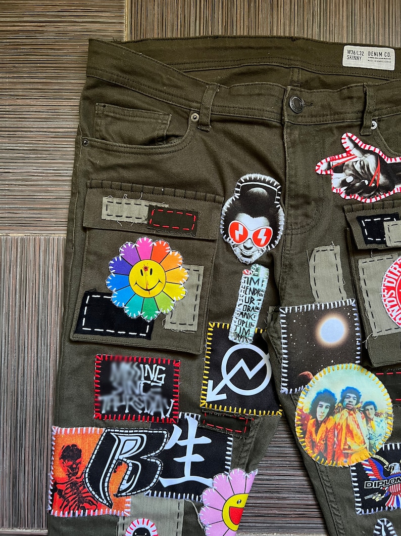 May include: Green cargo pants with various patches sewn on, including a smiley face flower, a red and white graphic, a moon, and a band photo. The pants have a label that reads "W36/L32 DENIM CO. SKINNY".