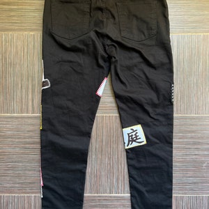 May include: Black jeans with colourful patches and a white patch with the Japanese character "度" on the right leg. The jeans have a black tag with the text "ZILLA KAMI" on the back.