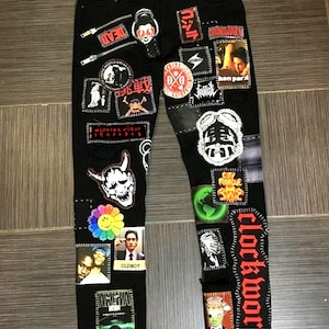 May include: Black denim jeans with various patches and embroidered designs. Patches include a skull, a flower, a cartoon character, and the words "clockwork" and "Oldboy".