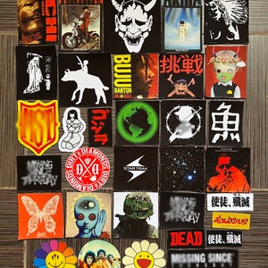 May include: A collection of colourful stickers featuring various designs, including anime characters, animals, and abstract patterns. The stickers are arranged in a grid on a wooden surface.