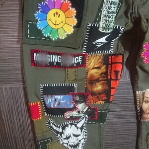May include: Green cargo pants with various patches sewn on, including a rainbow flower with a smiley face, a band patch with the text "WIZRD", a patch with the text "SING ICE", a patch with the text "THE KILLER", and a patch with the text "STAR", along with other patches.