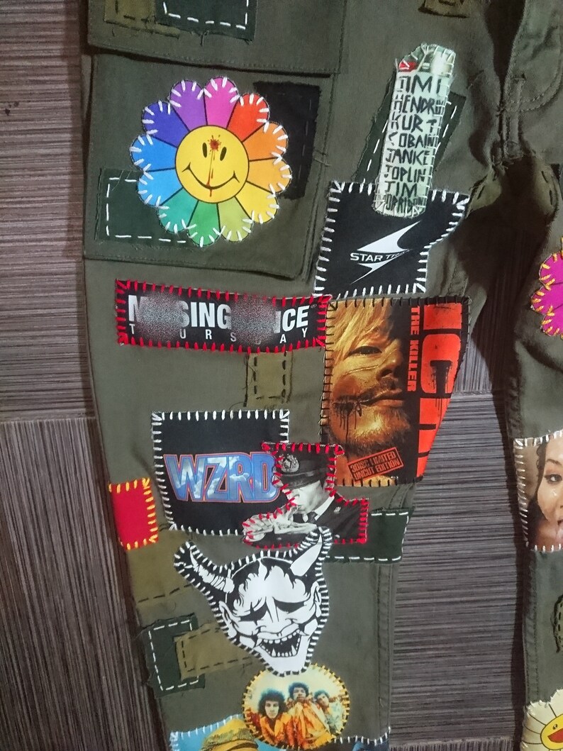 May include: Green cargo pants with various patches sewn on, including a rainbow flower with a smiley face, a band patch with the text "WIZRD", a patch with the text "SING ICE", a patch with the text "THE KILLER", and a patch with the text "STAR", along with other patches.