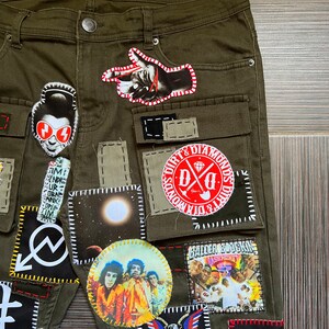 May include: Olive green cargo pants with various patches sewn on. Patches include a hand pointing, a moon, a band, a skull, and a logo that says "Dirt & Diamonds".