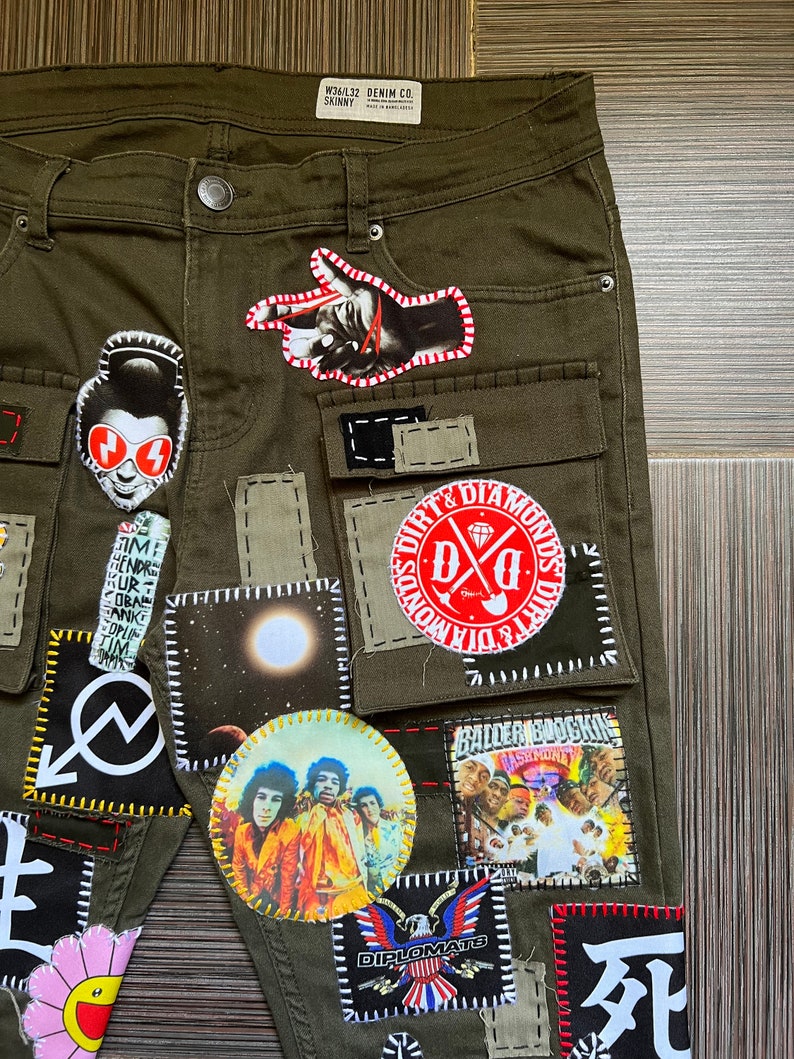 May include: Olive green cargo pants with various patches sewn on. Patches include a hand pointing, a moon, a band, a skull, and a logo that says "Dirt & Diamonds".
