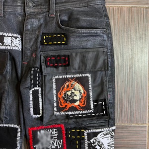 May include: Black denim jeans with multiple patches sewn on. The patches are various colors and feature different designs, including a face, a Native American headdress, and text.