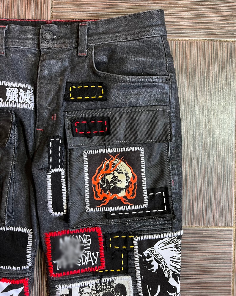 May include: Black denim jeans with multiple patches sewn on. The patches are various colors and feature different designs, including a face, a Native American headdress, and text.