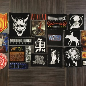 May include: A collection of 18 vintage stickers featuring various designs, including a demon, a motorcycle, a wizard, a Native American headdress, and Japanese characters. The stickers are on a wood-grain background.