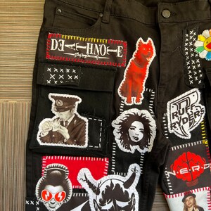May include: Black denim jeans with various patches sewn on, including a red dog, a black and white portrait of a man in a hat, a red and white demon, a black and white portrait of a woman, a red and white flower, and a black and white logo with the text "STAR TRAK".