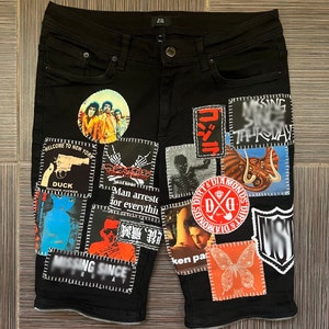 May include: Black denim shorts with various patches sewn on. Patches include a band logo, a skull, a butterfly, and a graphic of a gun. The text "Welcome to New York", "Duck", "Man arrested for everything", "Missing Since", "Dirt & Diamonds", and "T-Kmay" are visible on the patches.