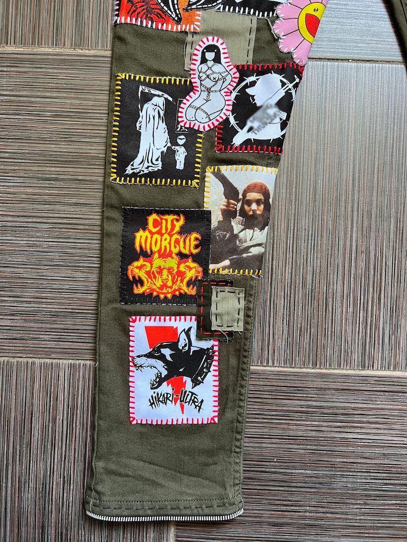 May include: Green cargo pants with various patches sewn on. Patches include a skull and crossbones, a woman in bondage, a grim reaper, a dog, and a person holding a gun. The text "City Morgue" and "Hikari Ultra" are visible on the patches.