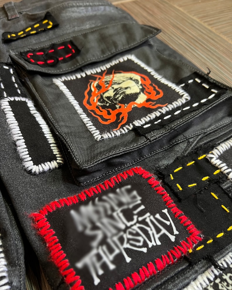 May include: Black denim pants with multiple patches sewn on. The patches are black, white, red, and yellow. One patch has a white graphic that says "Missing Since Thursday".