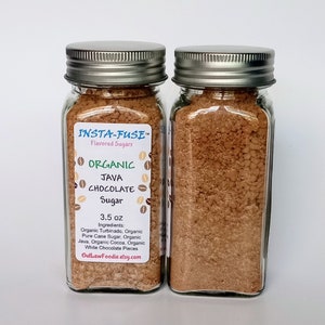 May include: Two glass jars filled with brown sugar. The jars have silver lids and labels that read "INSTA-FUSE Flavored Sugars" and "ORGANIC JAVA CHOCOLATE Sugar." The label also lists ingredients and the weight of 3.5 oz.
