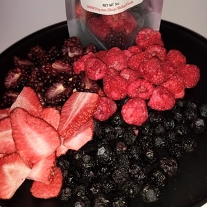 Pu&ograve; includere: Un piatto nero con una variet&agrave; di frutta liofilizzata, tra cui fragole, lamponi, more e mirtilli. Il testo sulla busta recita "Gourmet Freeze Dried Snacks, Candies, Drink Mixes & More. Net WT 1 oz. www.Etsy.com/Shop/OutlawFoodie"