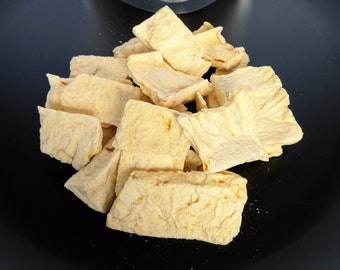 May include: A pile of dried pineapple slices on a black surface. The pineapple slices are light yellow and have a slightly translucent appearance.