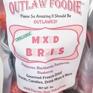 Pu&ograve; includere: Un sacchetto rosa e bianco con un'etichetta che recita "OUTLAW FOODIE" e "ORGANIC MIXED BERRIES". L'etichetta elenca anche gli ingredienti: fragole, more, lamponi, mirtilli. Il sacchetto contiene bacche liofilizzate e ha un peso netto di 1 oz.