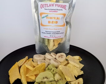 May include: A bag of organic freeze-dried tropical fruit blend with the text "OUTLAW FOODIE" and "Flavor So Amazing It Should Be OUTLAWED!" on the front. The bag contains pineapple, banana, mango, and kiwi. The fruit is arranged on a black plate.
