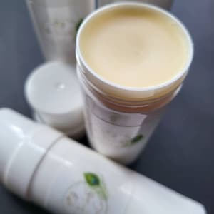 May include: Three white containers of natural body butter. The container in the center is open, revealing a light yellow, creamy texture.