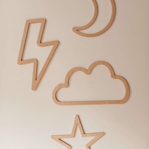 Peut inclure: Quatre décorations murales en bois en forme de croissant de lune, de nuage, d'éclair et d'étoile. Les pièces sont toutes en bois naturel et ont une couleur brun clair.