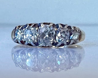May include: A gold band ring with five clear gemstones set in a row. The ring is on a white surface.