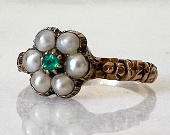 May include: A gold ring featuring a flower design set with pearls and a green gemstone in the centre.