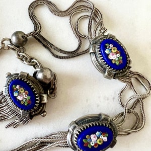 May include: A silver chain necklace with three oval pendants. Each pendant features a blue enamel background with a floral design in white, pink, yellow, and green.