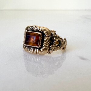 May include: A gold ring with an ornate design and a rectangular amber stone.