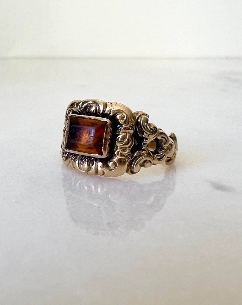 May include: A gold ring with an ornate design and a rectangular amber stone.