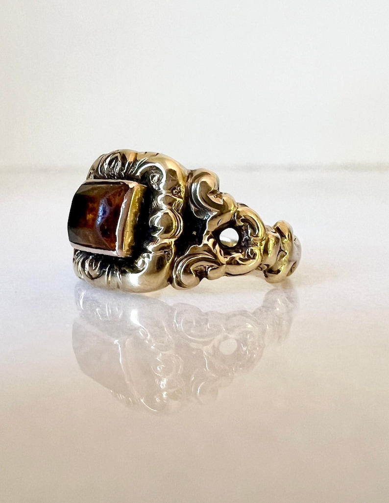 May include: A gold ring with an ornate design and a rectangular amber stone.