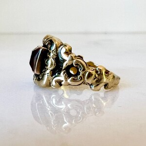 May include: A gold ring featuring a large, dark red gemstone set within an intricate, ornate design.