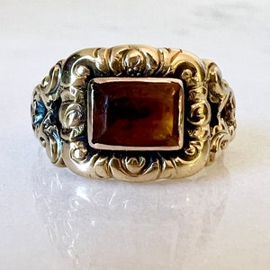 May include: A gold ring with an ornate design and a brown rectangular gemstone.