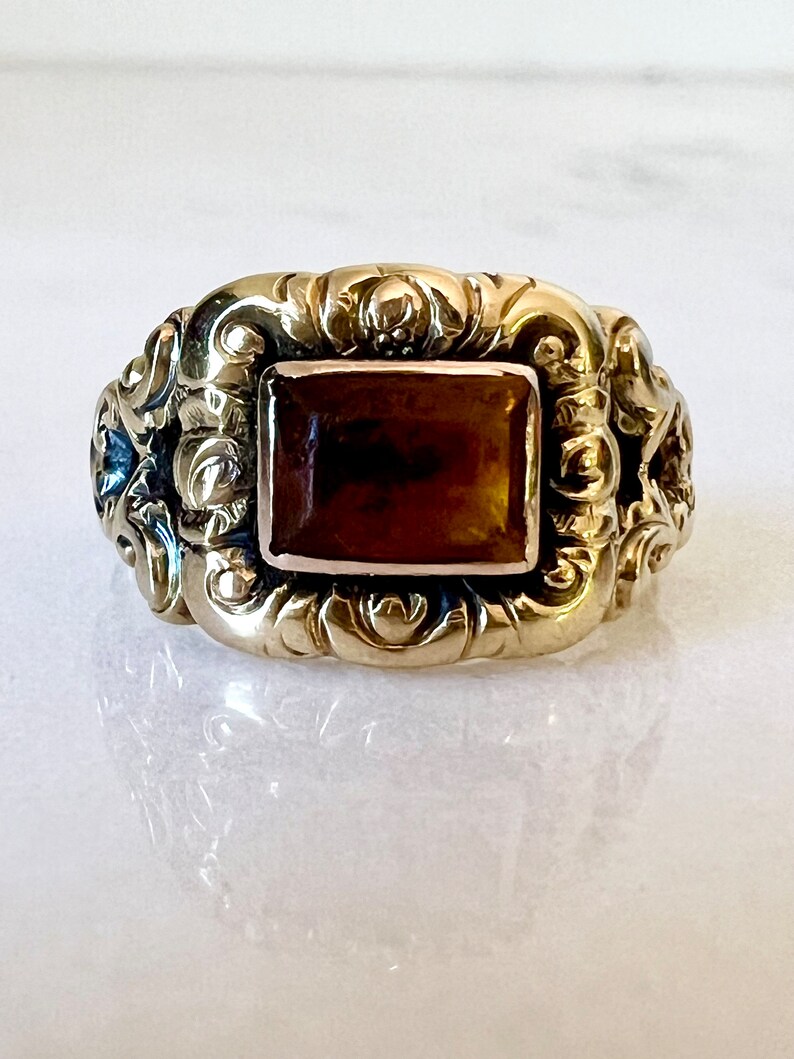 May include: A gold ring with an ornate design and a brown rectangular gemstone.