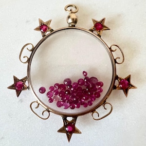 May include: A gold pendant with a circular frame and a scattering of red rubies inside. The frame is decorated with eight gold stars, each with a red ruby in the centre.