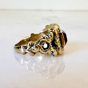 May include: A gold ring with an ornate design and a large, faceted, reddish-purple gemstone.