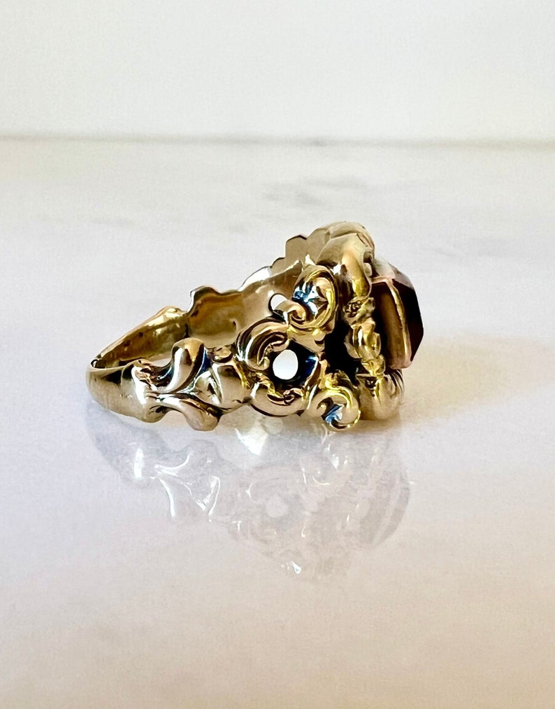 May include: A gold ring with an ornate design and a large, faceted, reddish-purple gemstone.